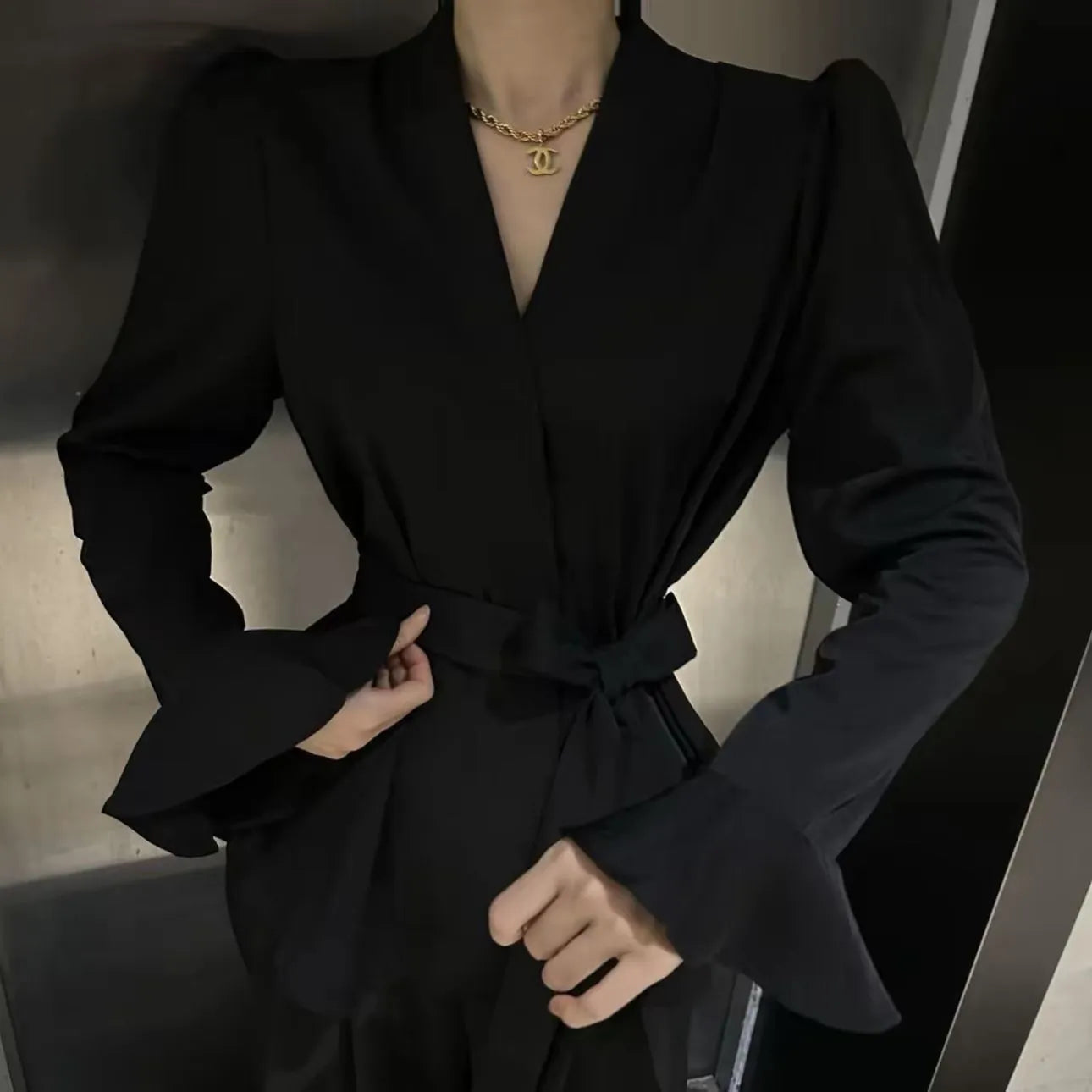 Women's black French-style shirt with an irregular collar and long bell sleeves, showing the tied front closure.