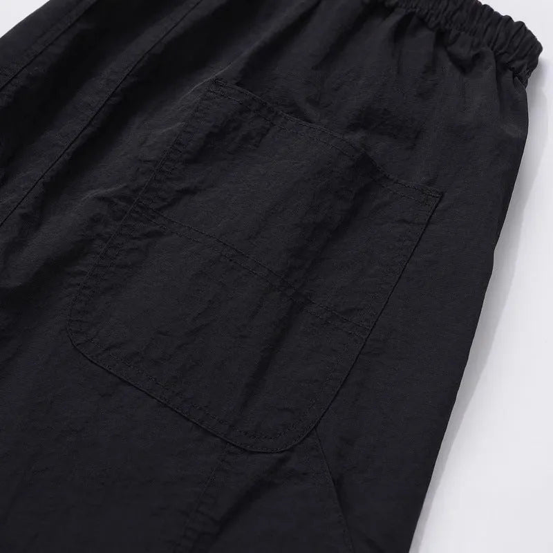 Men's baggy paratrooper pants in black with elastic waist and drawstring, side view on model