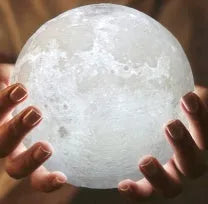 3D printed white moon lamp on a wooden stand with a glowing centre.