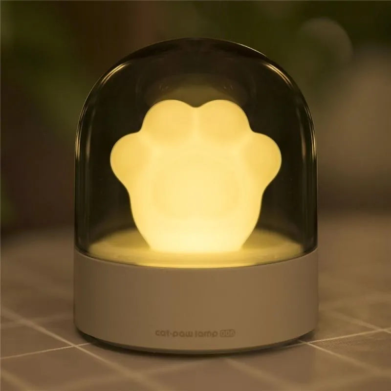 Grey cat paw shaped musical night light with USB charging cable on wooden desktop