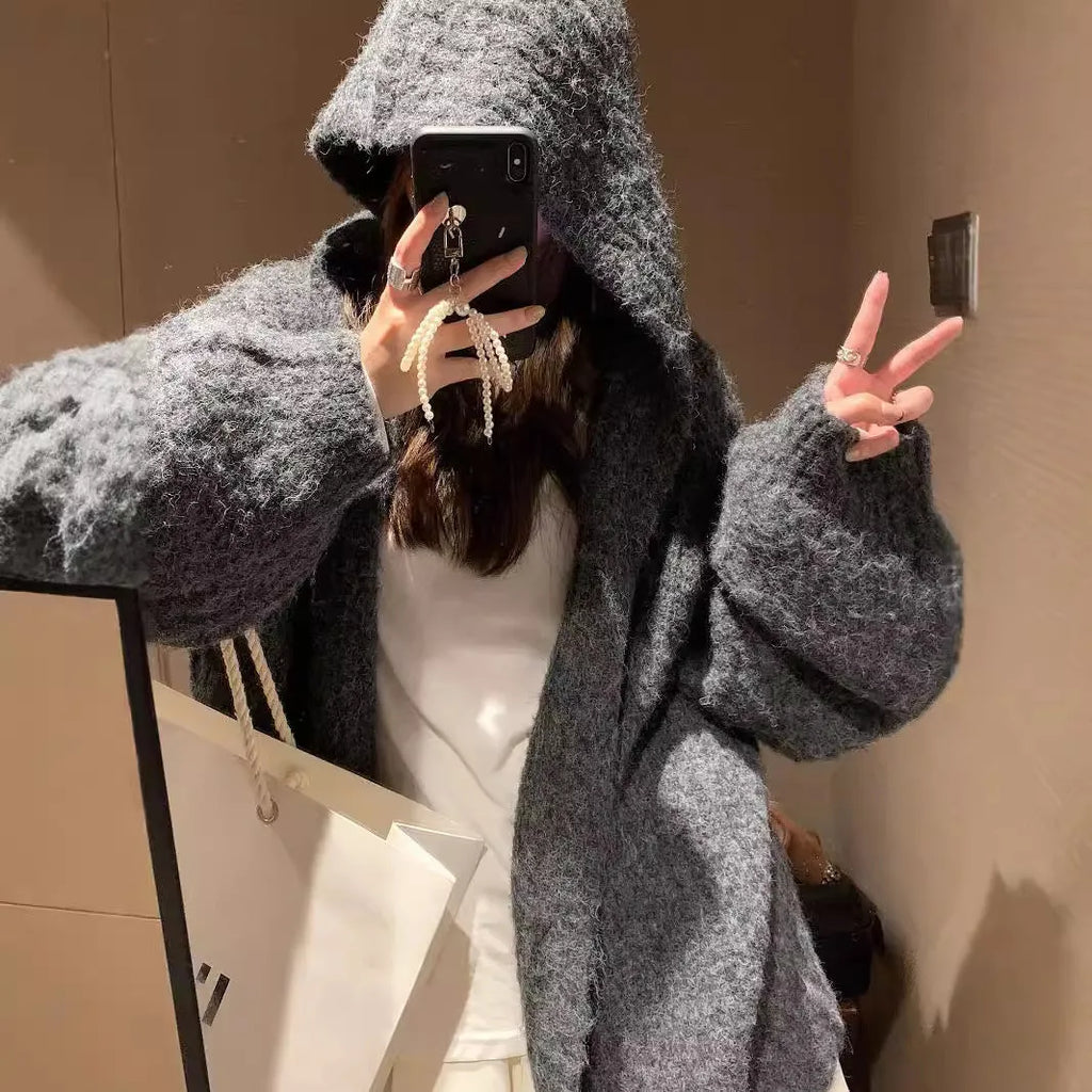 A woman wearing a thick, dark grey hooded cardigan with a loose fit and regular sleeves.