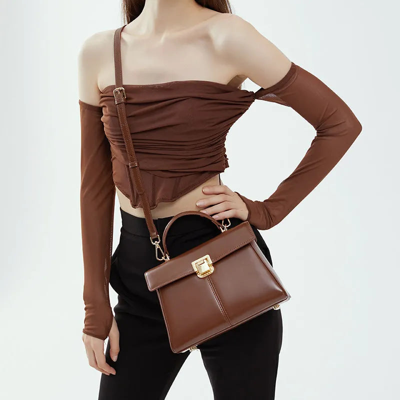 Black leather women's shoulder bag with vachette clasp showing square shape and adjustable strap.