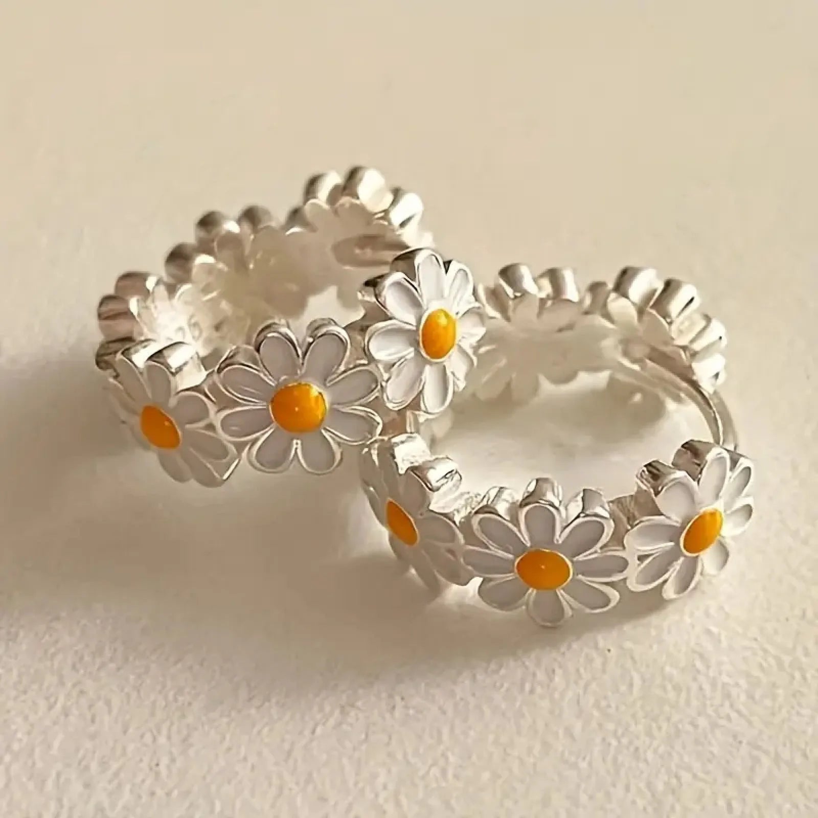 A pair of white daisy flower ring earrings with inlaid gems, shown on a plain background.