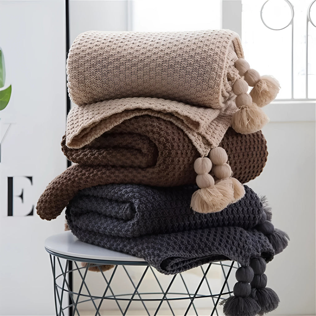 Nordic fringed knit ball acrylic blanket in beige, 130x170cm, draped on a sofa