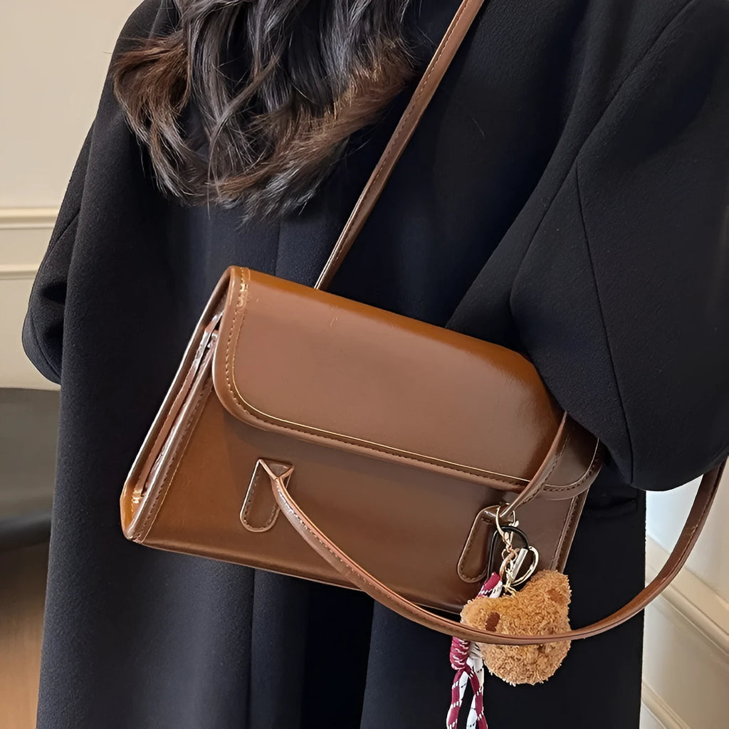 Brown women's PU leather square shoulder bag with double straps and a matching tassel pendant on a table.