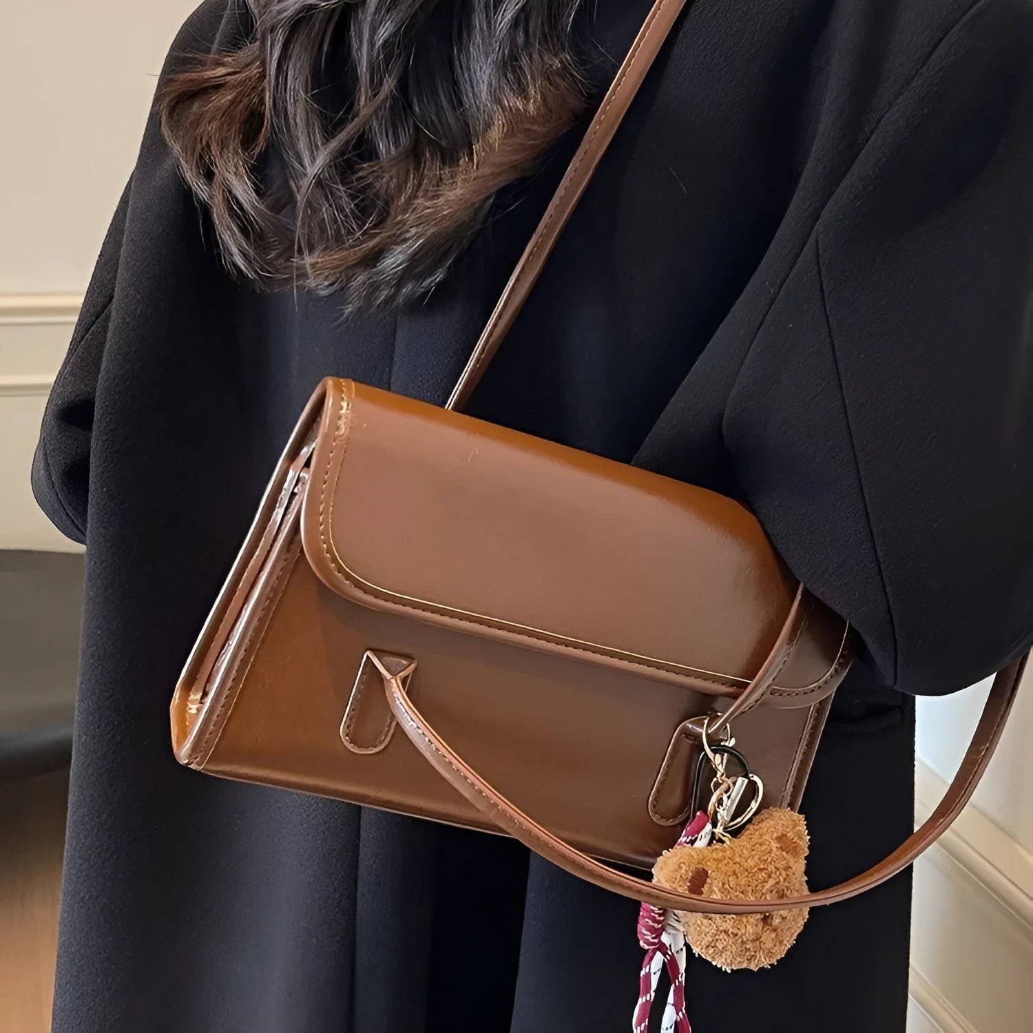 Brown women's PU leather square shoulder bag with double straps and a matching tassel pendant on a table.