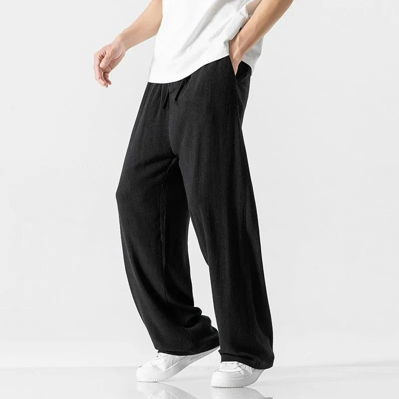 Men's beige loose straight-leg linen trousers with a drawstring waist on a neutral background.