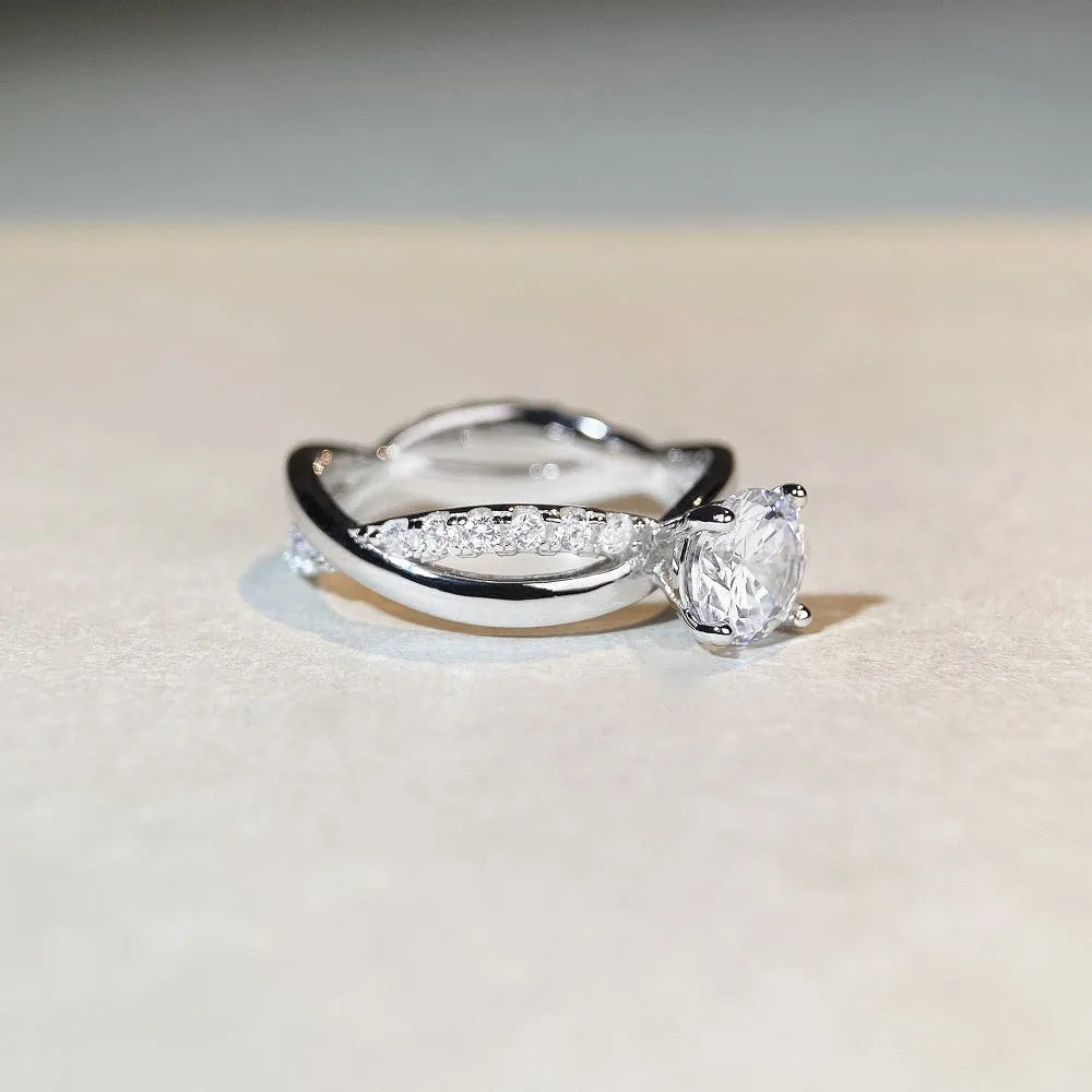 Close-up of a silver ring with a 1 karat moissanite in a four-claw setting, geometric cross design, and twisted band.