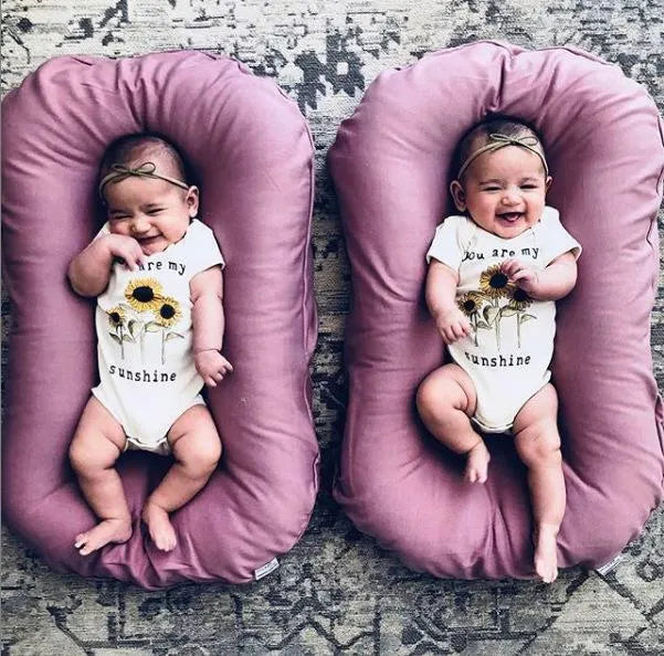 Beige portable cotton baby nest crib for infants on a neutral background.