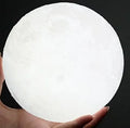 3D printed white moon lamp on a wooden stand with a glowing centre.