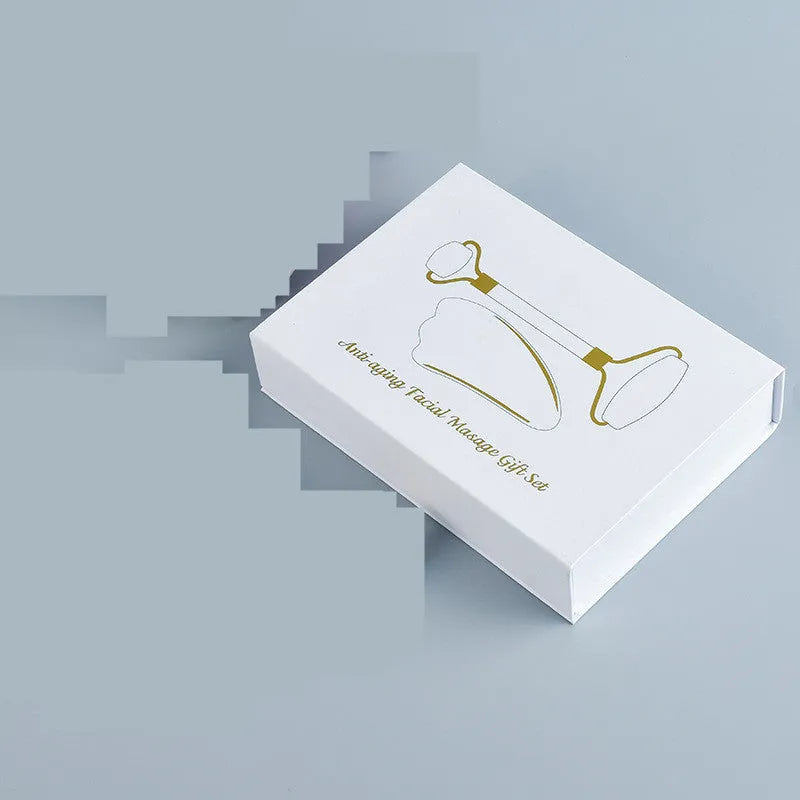 White jade facial roller and Gua Sha scraping board set on a plain surface.