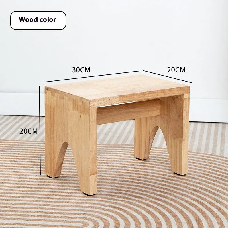 Solid wood distressed finish changing stool with bracket legs on a wooden floor.