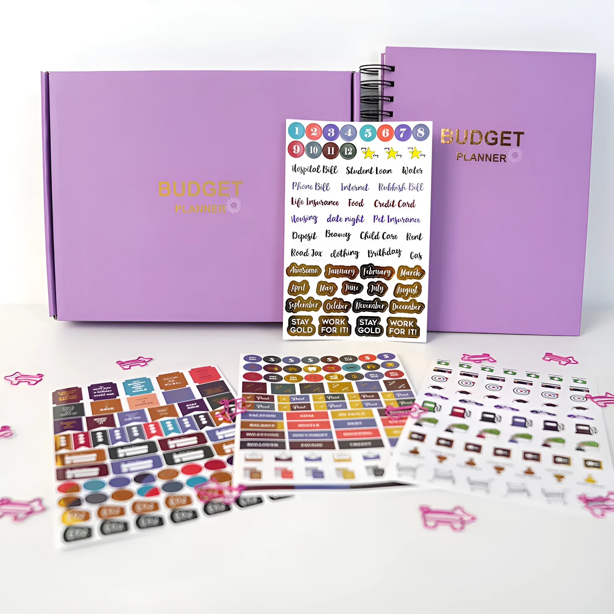 Purple coil-bound financial planning notebook open on a desk with pen, stickers, and paper clips.