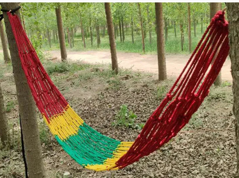 Nylon rope mesh hammock hung between two trees in a garden setting.