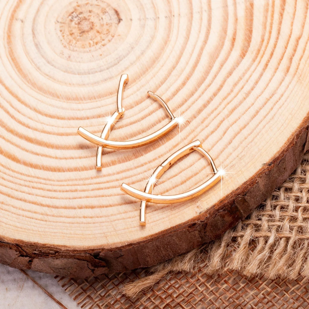 A pair of rose gold plated copper earrings in a cross shape on a plain background.