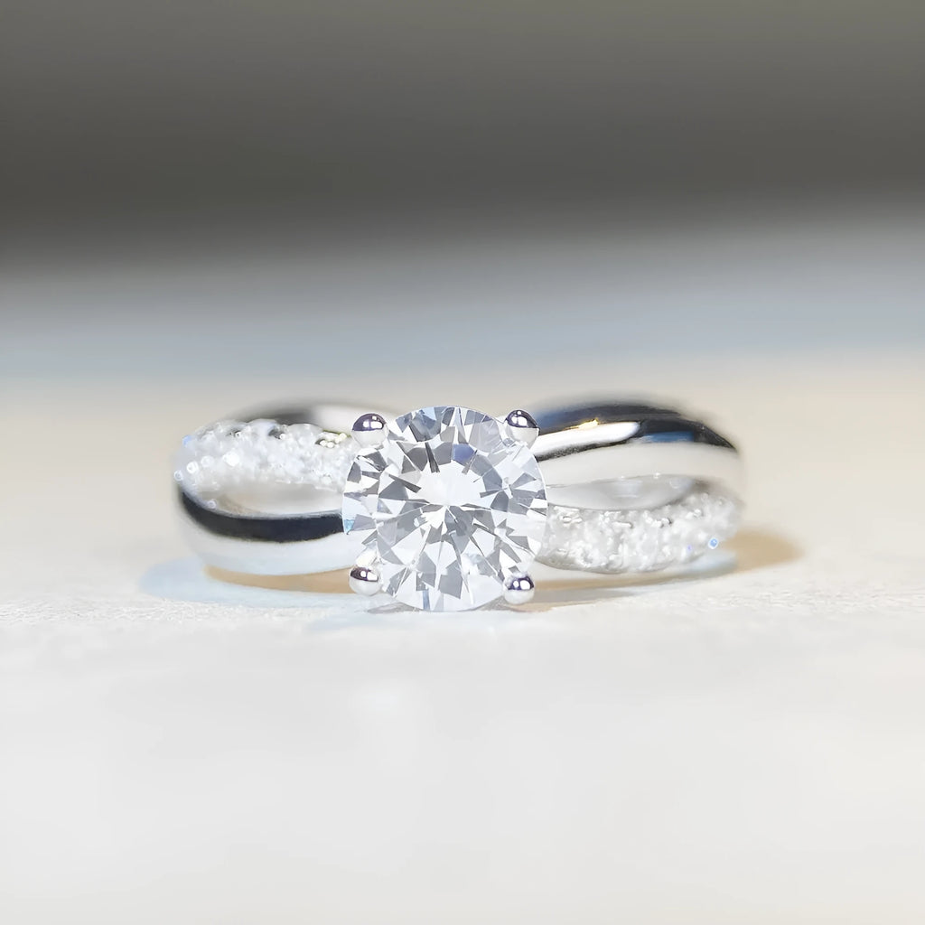 Close-up of a silver ring with a 1 karat moissanite in a four-claw setting, geometric cross design, and twisted band.
