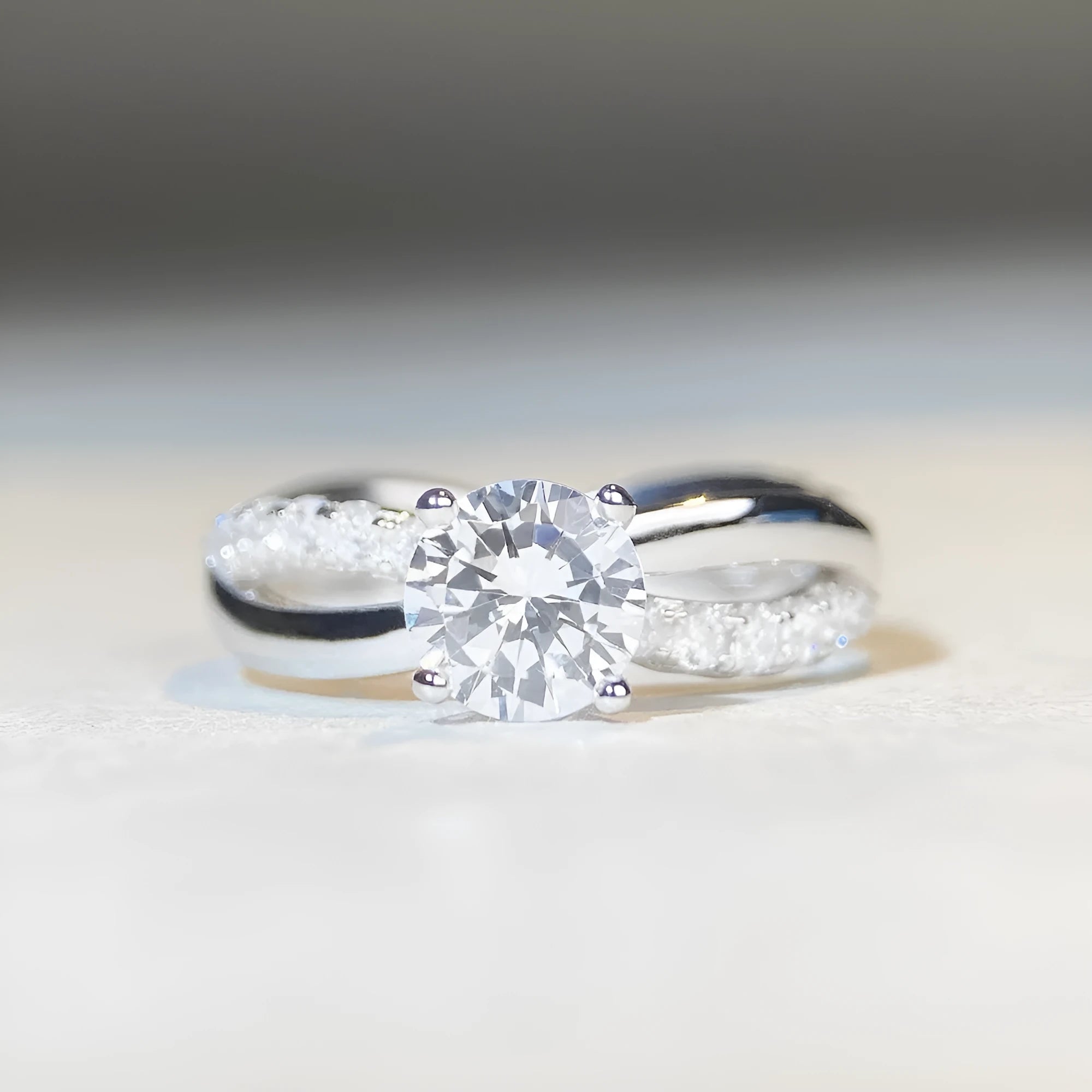 Close-up of a silver ring with a 1 karat moissanite in a four-claw setting, geometric cross design, and twisted band.