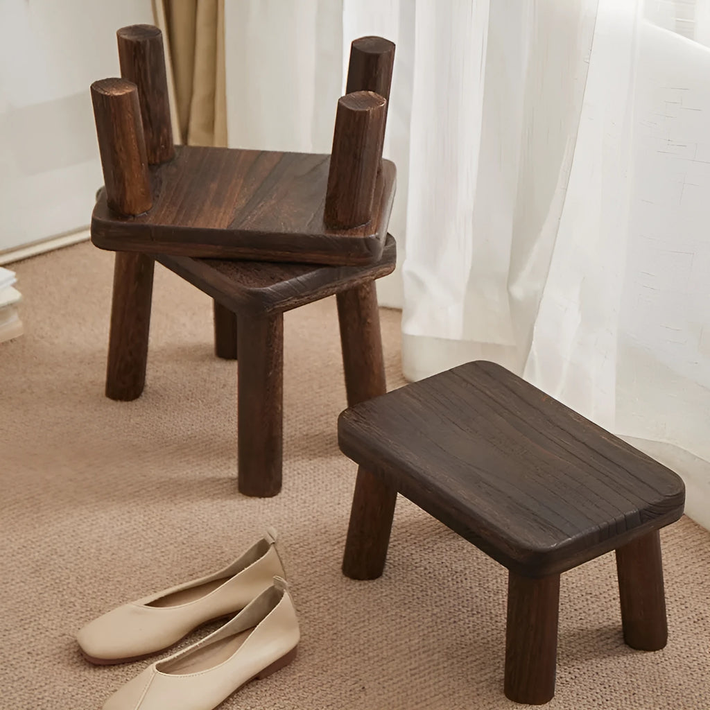 Solid wood distressed finish changing stool with bracket legs on a wooden floor.