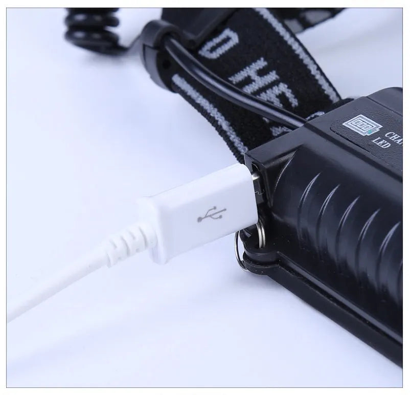 Fixed focus camping head torch with long range beam on a headband, shown with its rechargeable battery and charger.