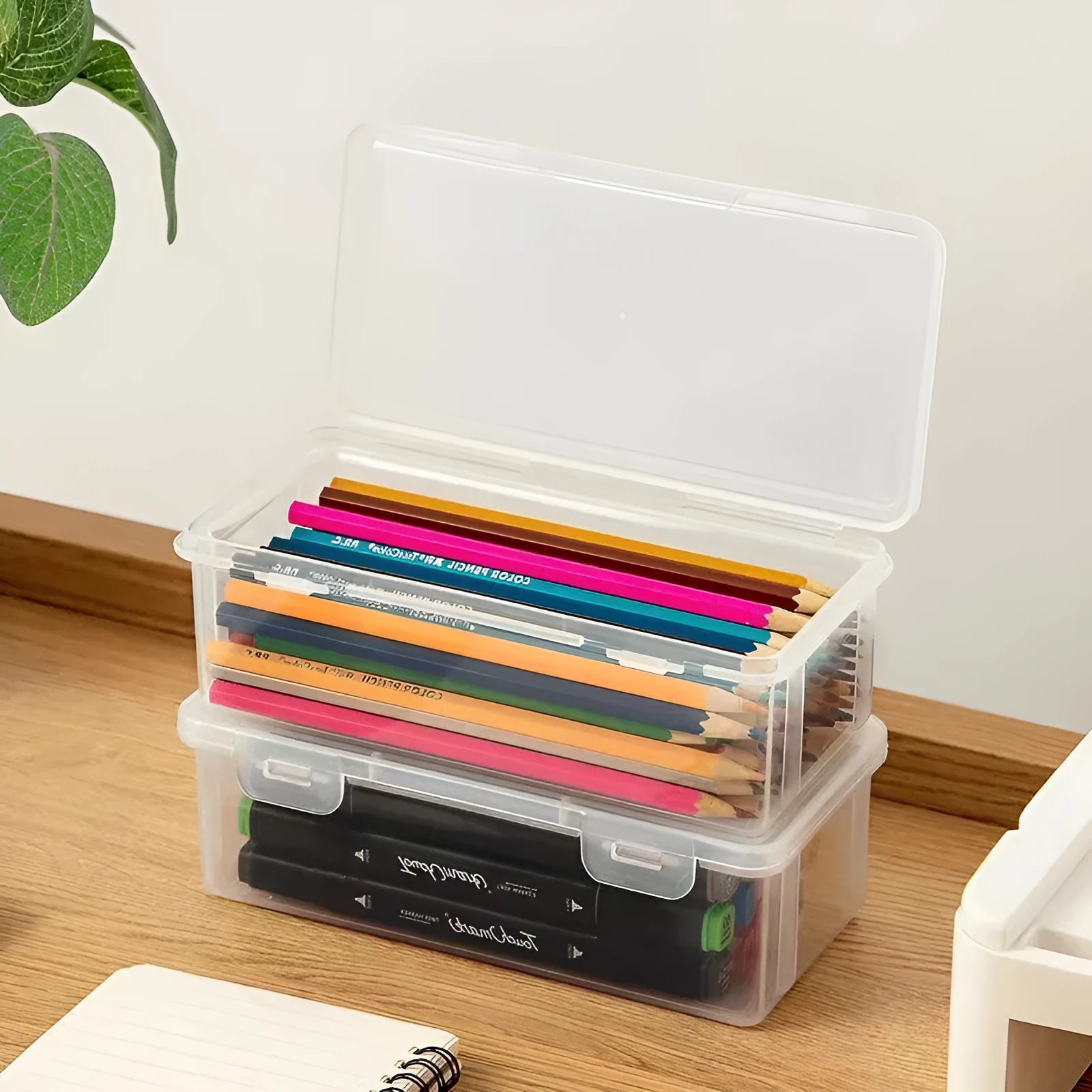 Clear plastic stationery storage box full of coloured pencils and drawing tools on a table.
