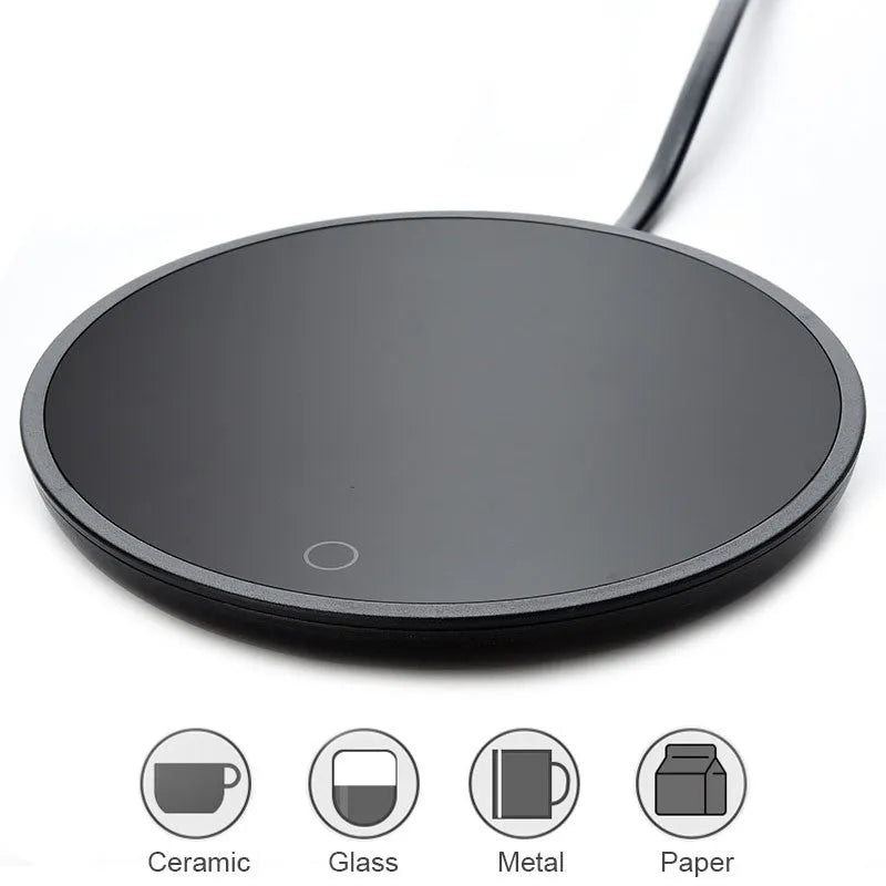 Black circular mug warmer with temperature switch, 12cm in diameter, on a desk next to a coffee cup.