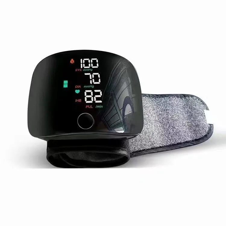 Black wrist blood pressure monitor with USB charging cable on a table.