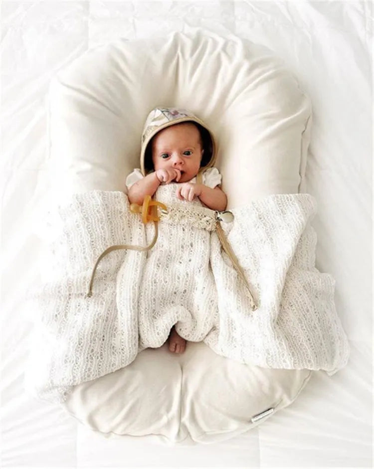 Beige portable cotton baby nest crib for infants on a neutral background.