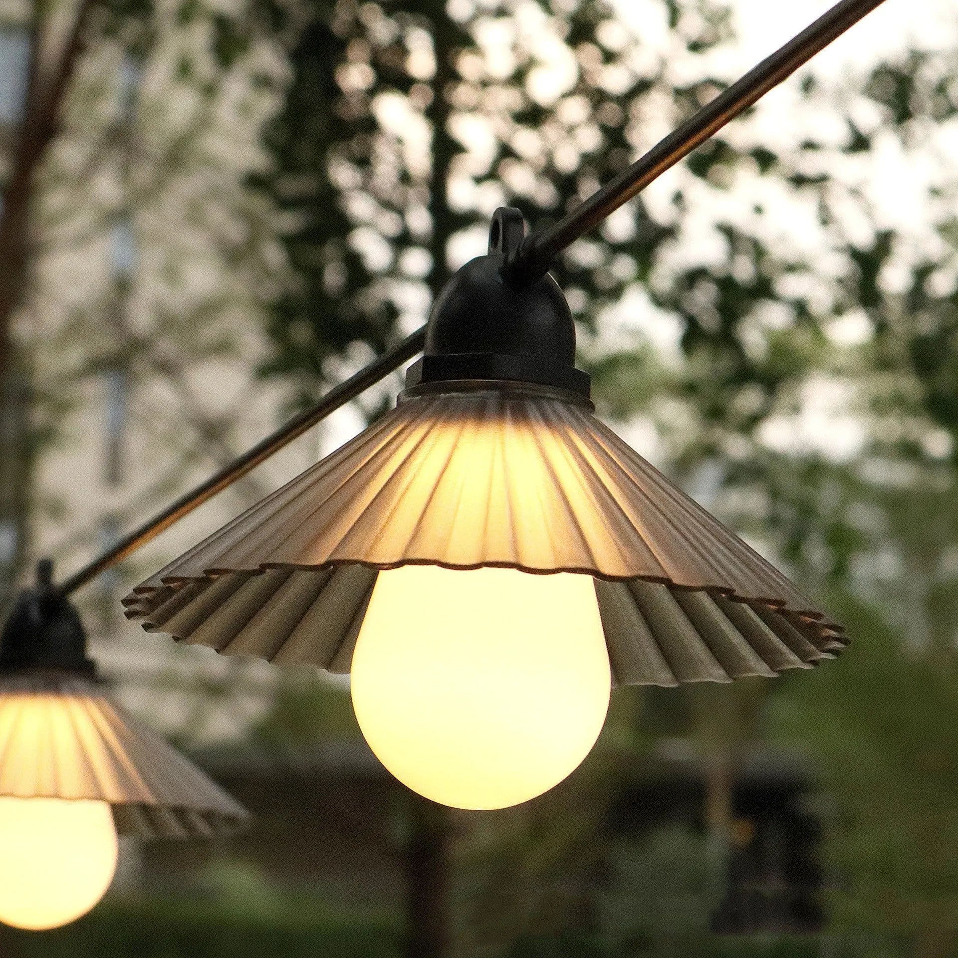 Outdoor LED string lights with flower-shaped globes in four colours, hanging in a garden.