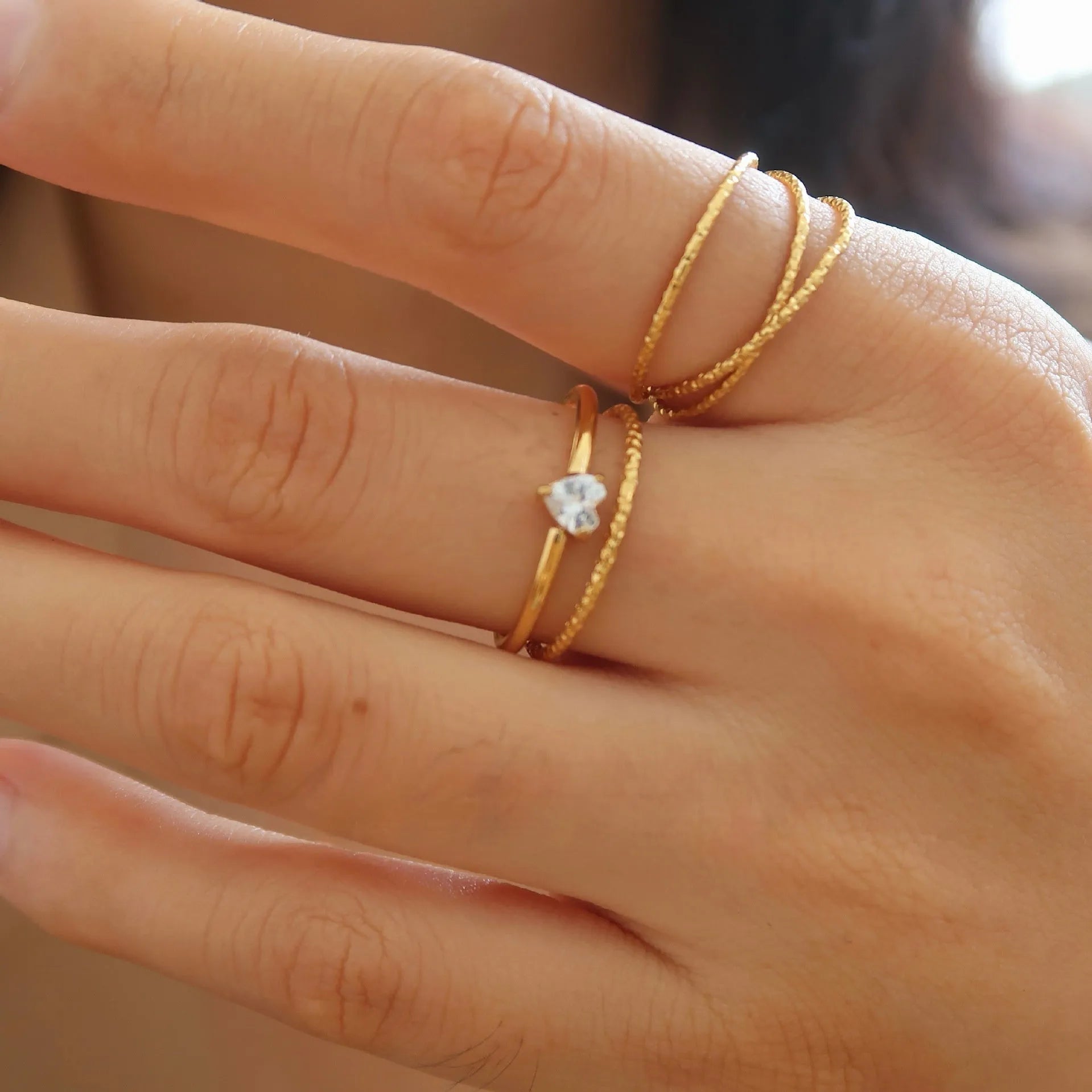 Golden electroplated stainless steel ring showing heart shape and oval charm design on female hand