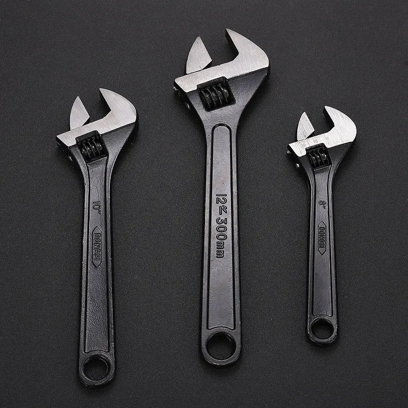 Blackened high carbon steel adjustable open-end wrench on a workbench, jaw set to mid-opening.