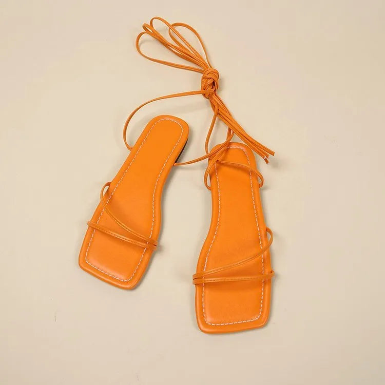 Women's flat sandals with ankle bandage detail and square toe in black, white, or orange.