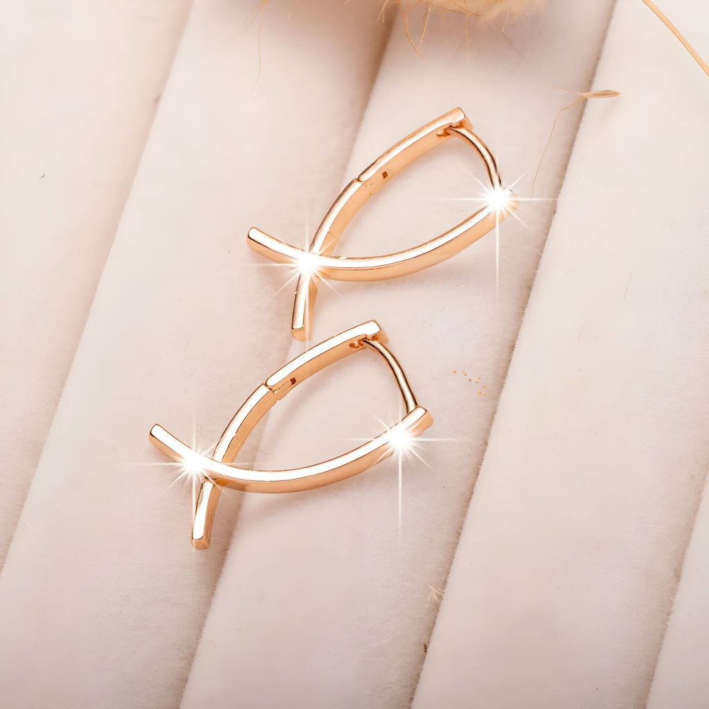 A pair of rose gold plated copper earrings in a cross shape on a plain background.