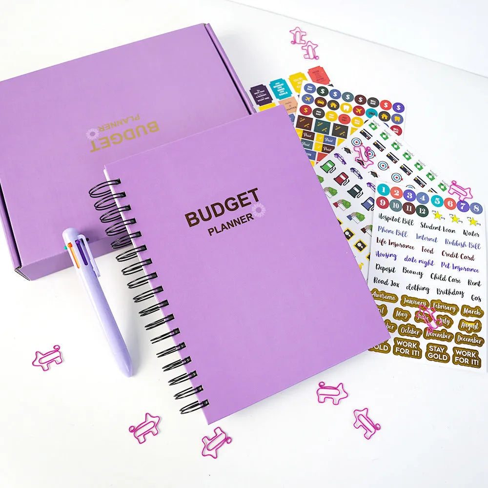 Purple coil-bound financial planning notebook open on a desk with pen, stickers, and paper clips.