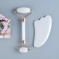 White jade facial roller and Gua Sha scraping board set on a plain surface.