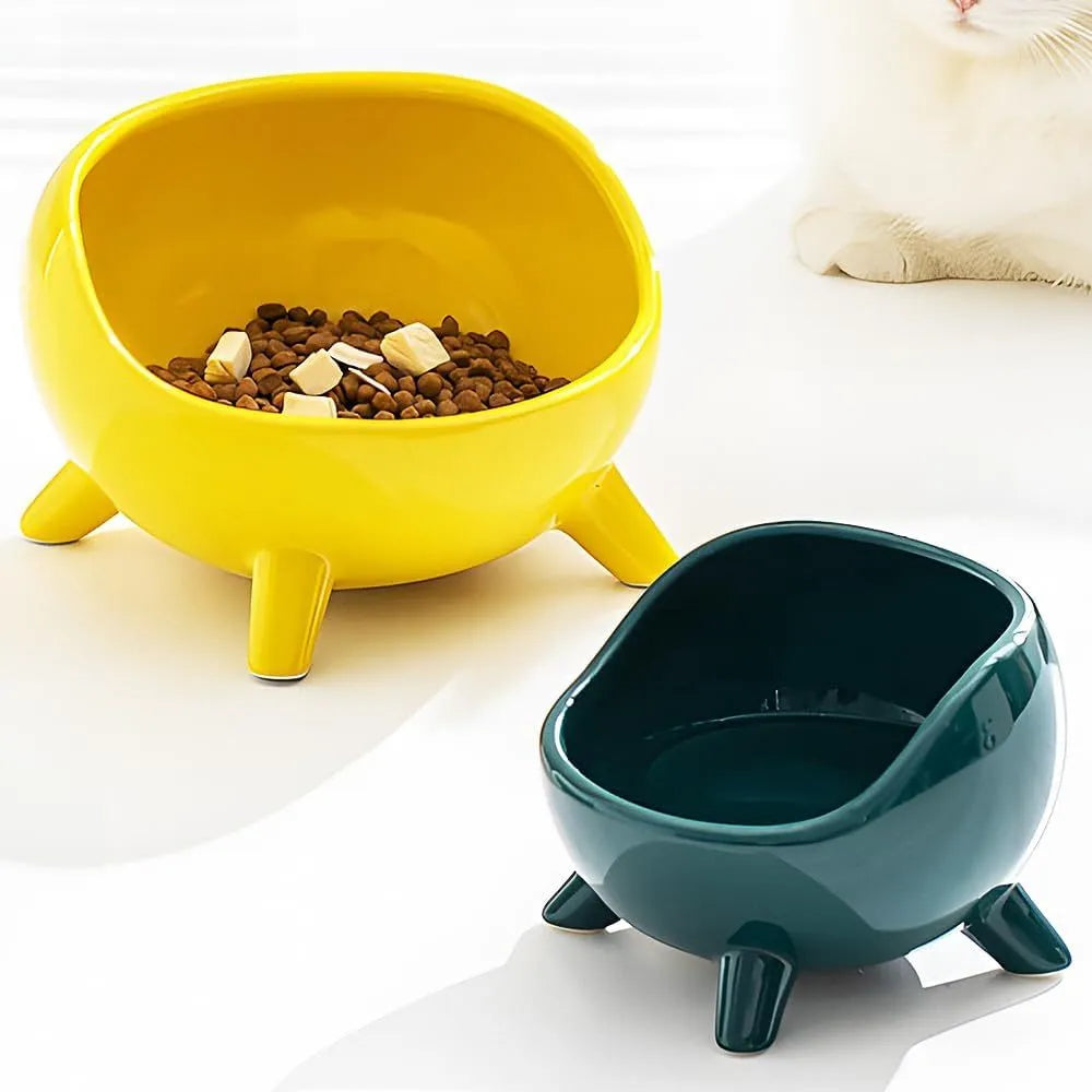 Green ceramic cat food bowl with four legs, wide mouth, and rounded arc shape on a light floor