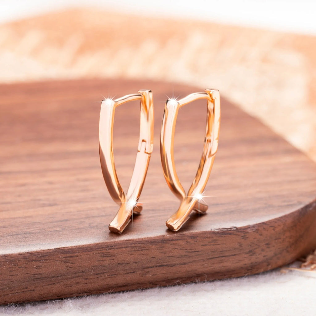 A pair of rose gold plated copper earrings in a cross shape on a plain background.