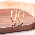 A pair of rose gold plated copper earrings in a cross shape on a plain background.