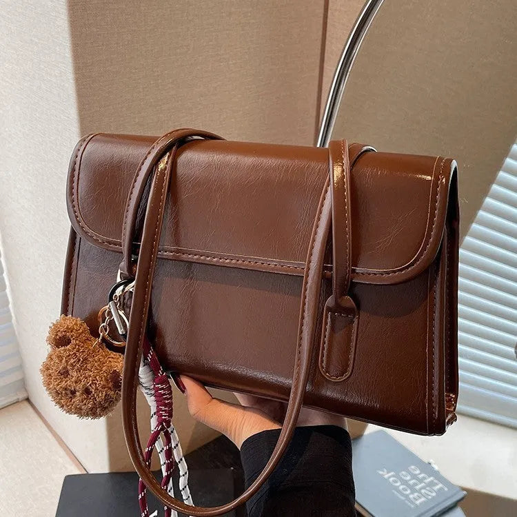 Brown women's PU leather square shoulder bag with double straps and a matching tassel pendant on a table.