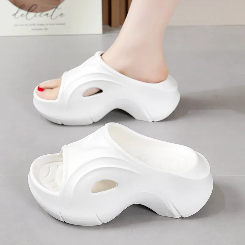 Women's white thick-soled EVA slippers with round toe on a sandy beach.