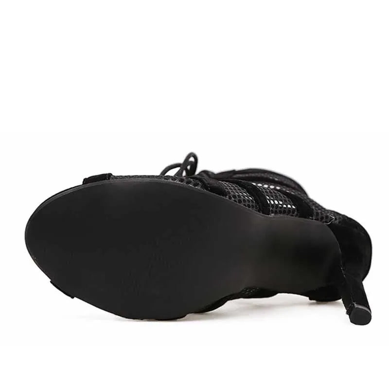 Black suede women's lace-up high heel shoes with a tall heel on a wooden floor.