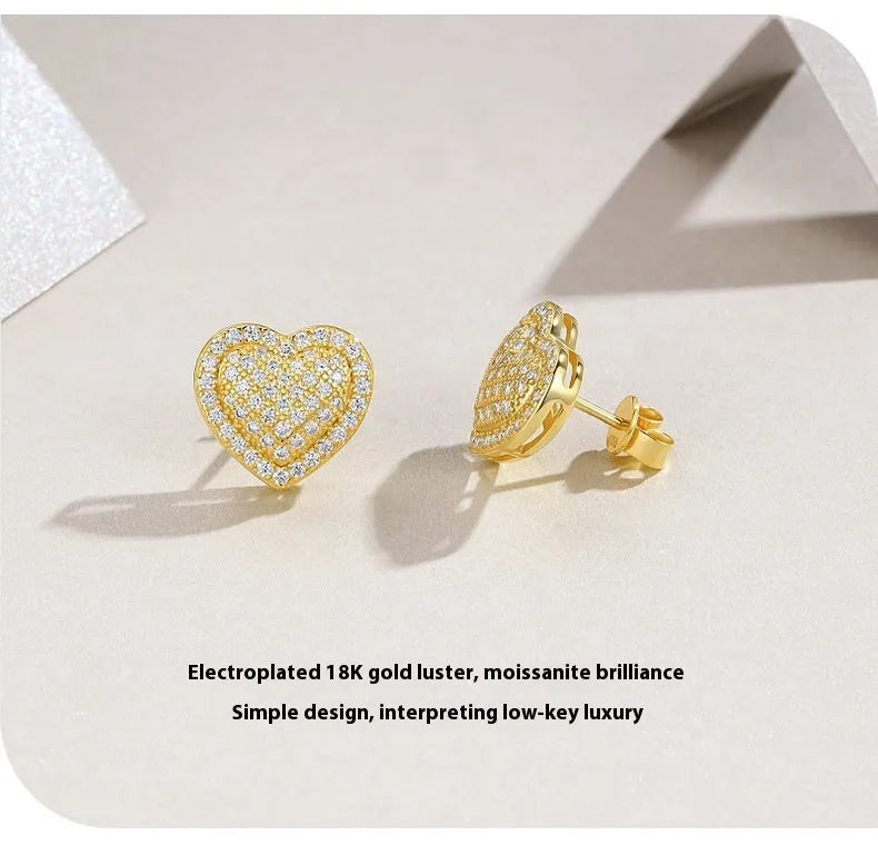 Golden heart-shaped stud earrings with moissanite centre on silver background