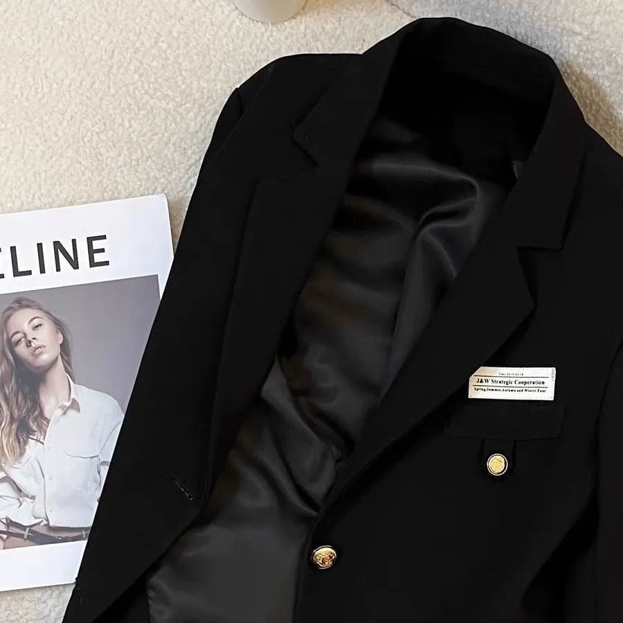 Women's black loose-fit short suit coat with long sleeves and pockets, shown on a hanger.