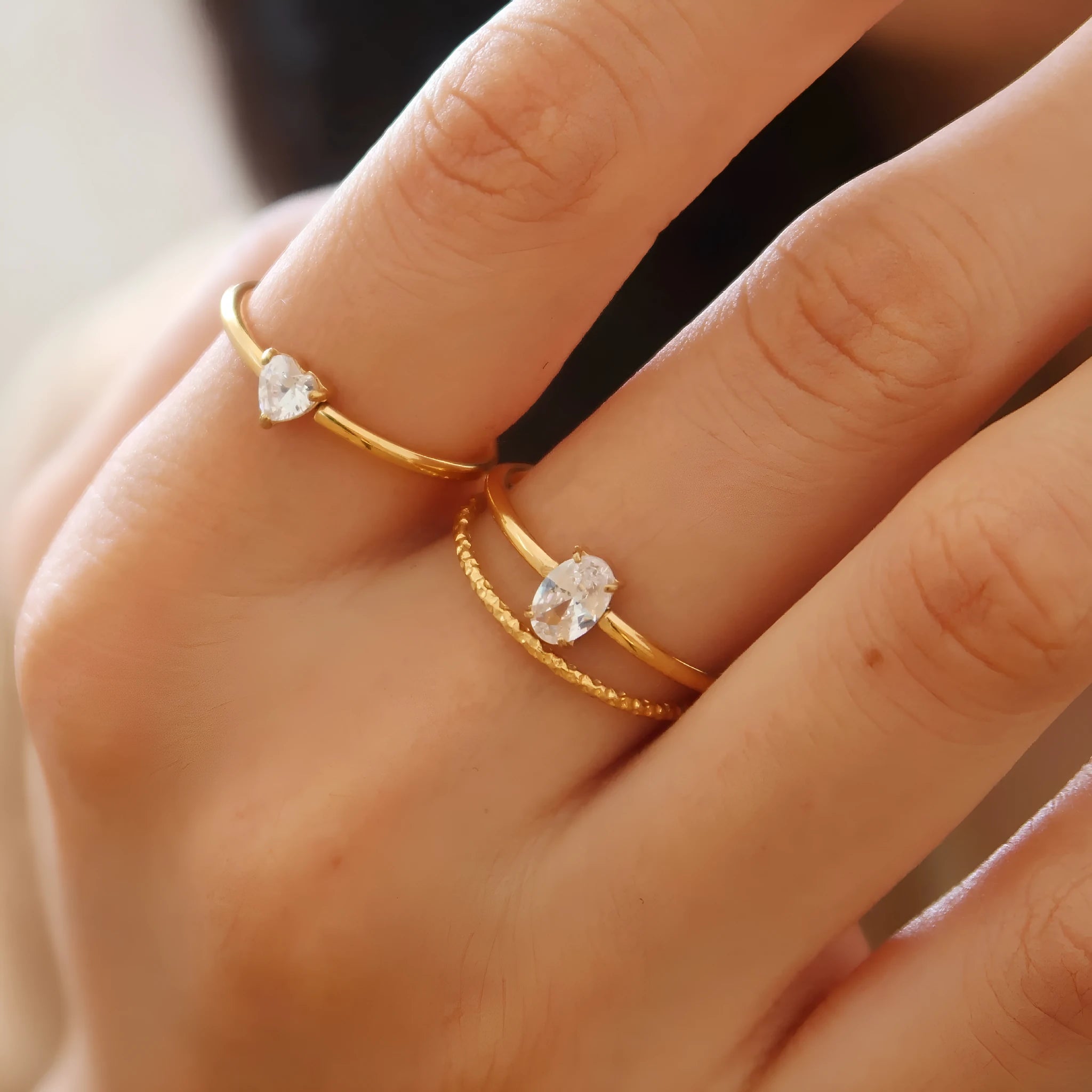 Golden electroplated stainless steel ring showing heart shape and oval charm design on female hand