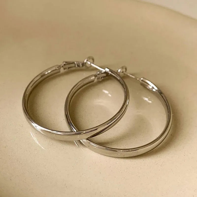 A pair of large, circular gold metal hoop earrings on a flat surface.