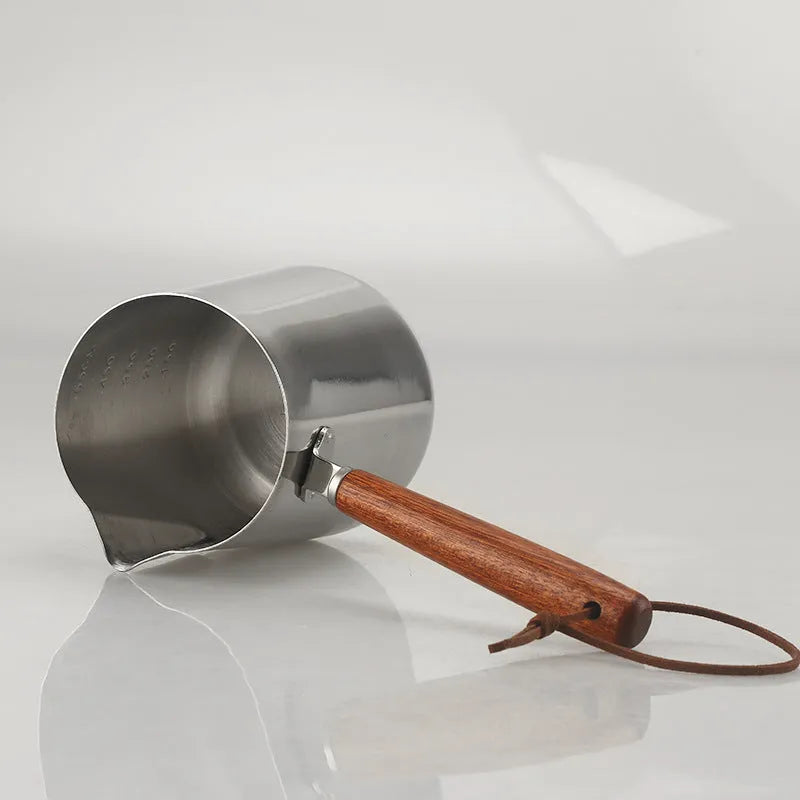 Stainless steel garland-spout milk jug with wooden handle showing measurement scale, for barista use.
