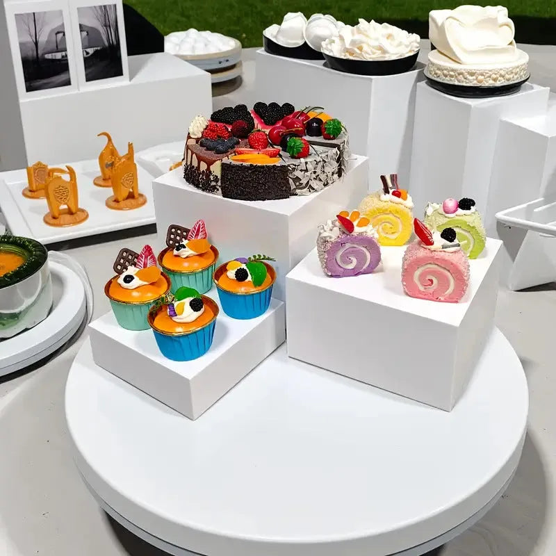 Six white plastic cube-shaped dessert display stands arranged in two rows for patisserie presentation