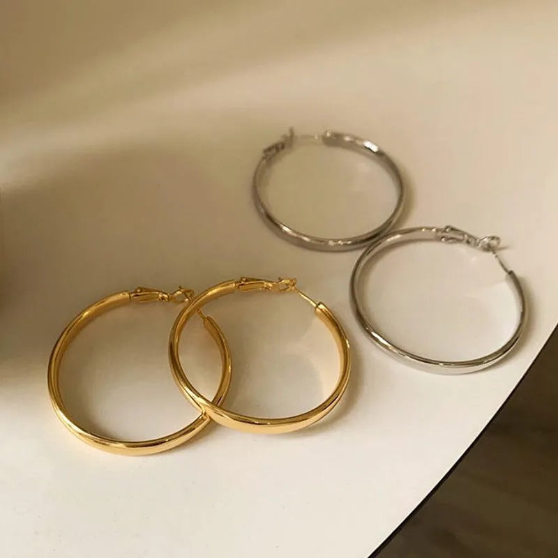A pair of large, circular gold metal hoop earrings on a flat surface.