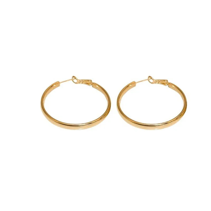 A pair of large, circular gold metal hoop earrings on a flat surface.