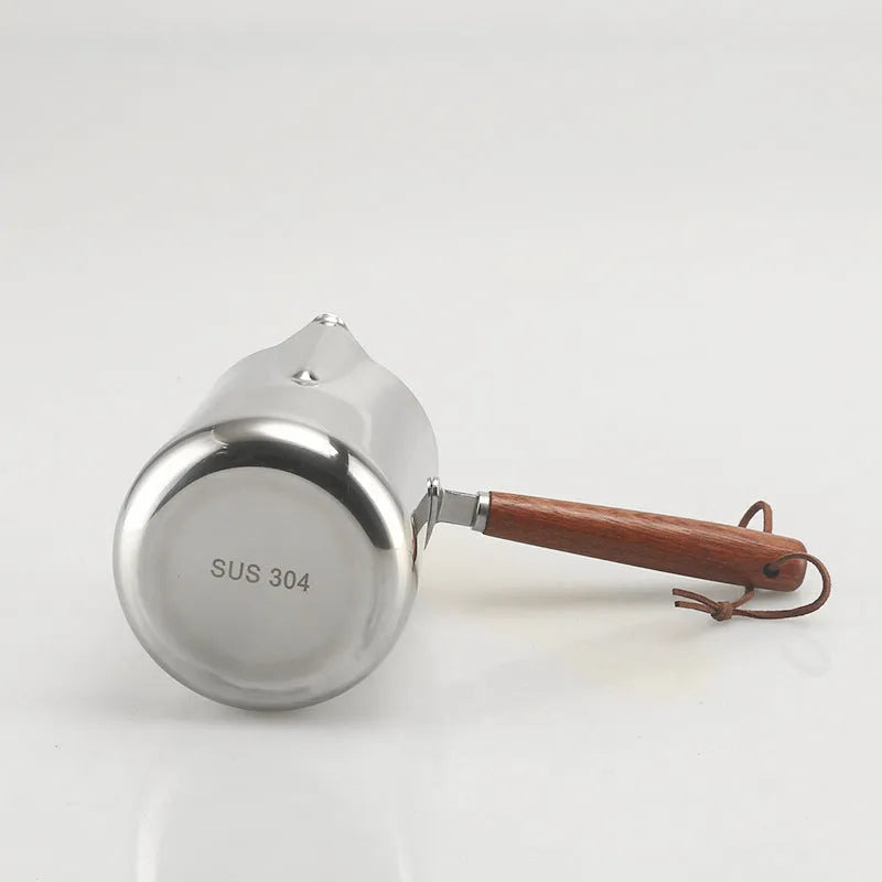 Stainless steel garland-spout milk jug with wooden handle showing measurement scale, for barista use.