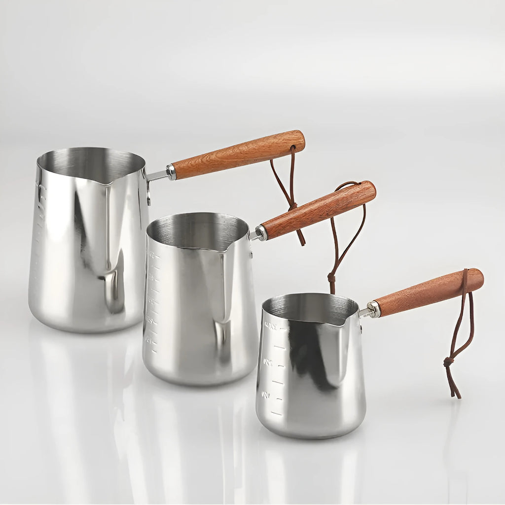Stainless steel garland-spout milk jug with wooden handle showing measurement scale, for barista use.